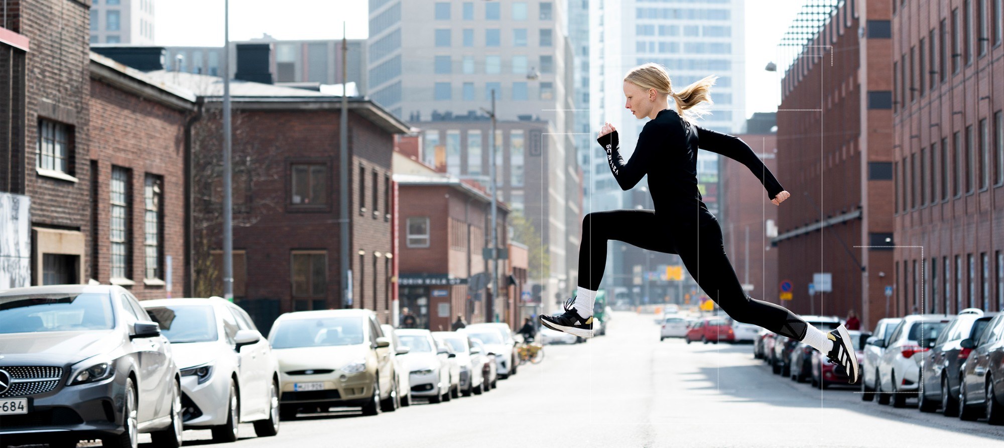 A runner in black mid-stride across a city street, traced by thin white measurement frames